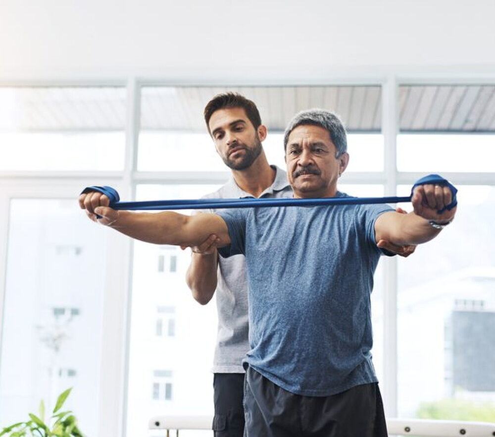 A therapist guiding an older patient through a resistance band exercise in a bright clinic