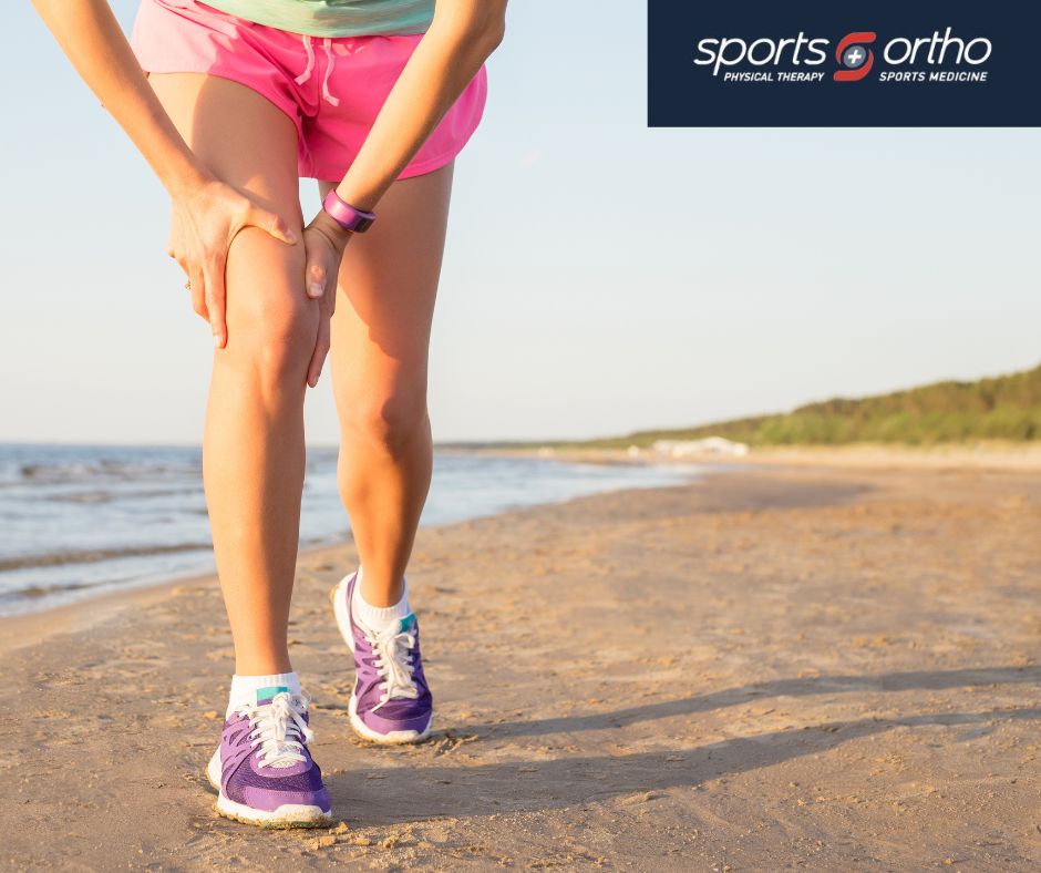 A person in athletic attire holding their knee in discomfort while running on a sandy beach, showcasing issues addressed by sports orthopedics and physical therapy.